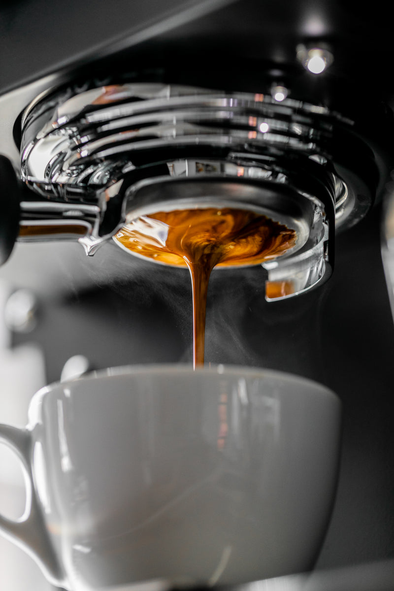Espresso being poured from a machine into a white cup.